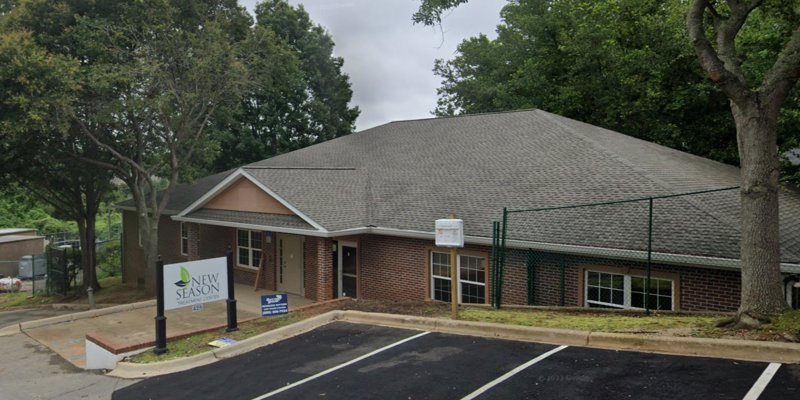 A peaceful brick building nestled among trees with a sign for New Season Treatment Center, offering a calm and inviting environment for visitors.