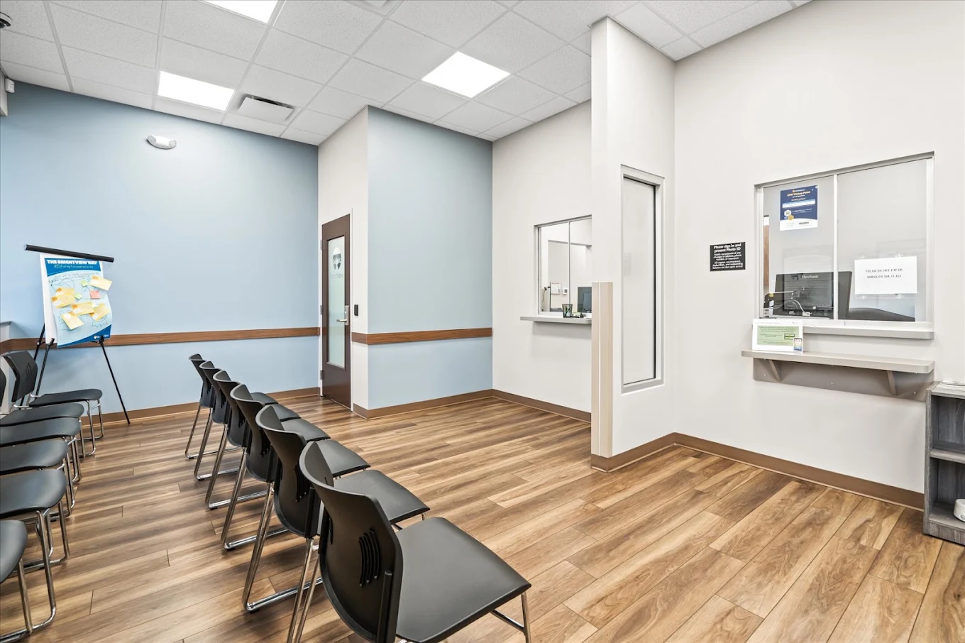 BrightView Health check-in area with rows of black chairs, service windows, blue accent walls, and wood-look flooring