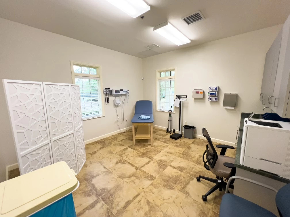 Clinical treatment room with exam chair, medical equipment, privacy divider, and workspace