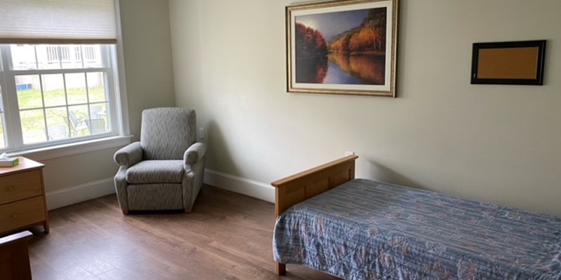 A peaceful bedroom with natural light, a cozy armchair, and simple furnishings, offering a serene space for rest and relaxation.