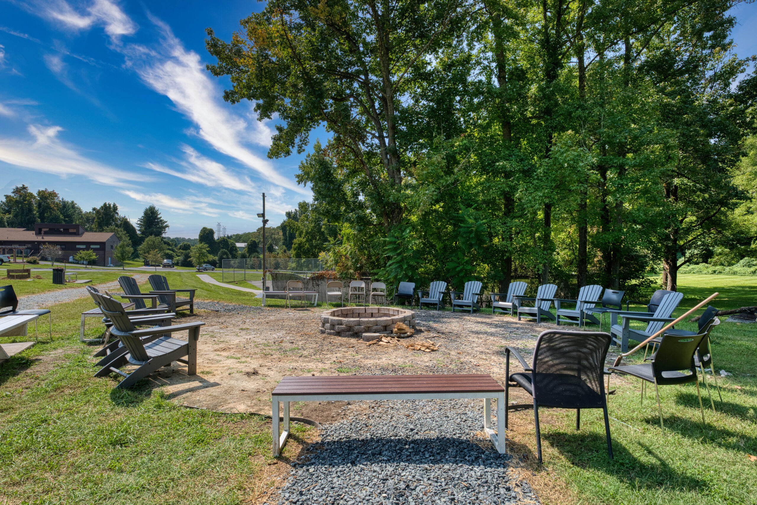 Outdoor firepit area with circle of chairs and surrounding trees.