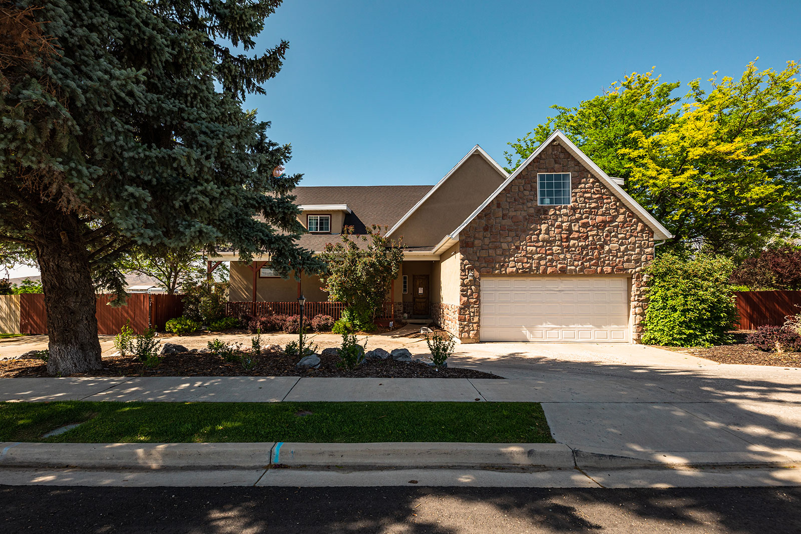 Front view of stone and tan house with garage and trees