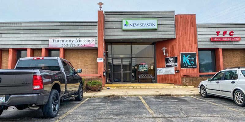 A small plaza featuring businesses like Harmony Massage, New Season, and TFC Fitness Training Center, with parked vehicles in front.