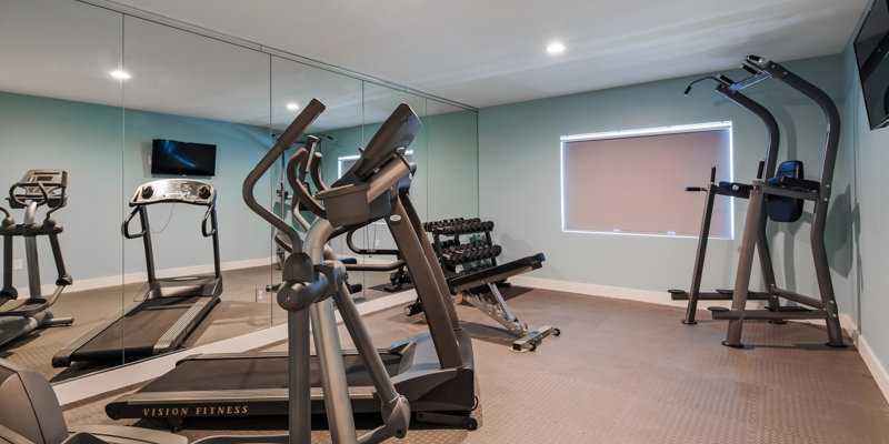 A well-equipped fitness room featuring treadmills, free weights, and exercise machines, complemented by mirrored walls and soft lighting for an energizing workout space.