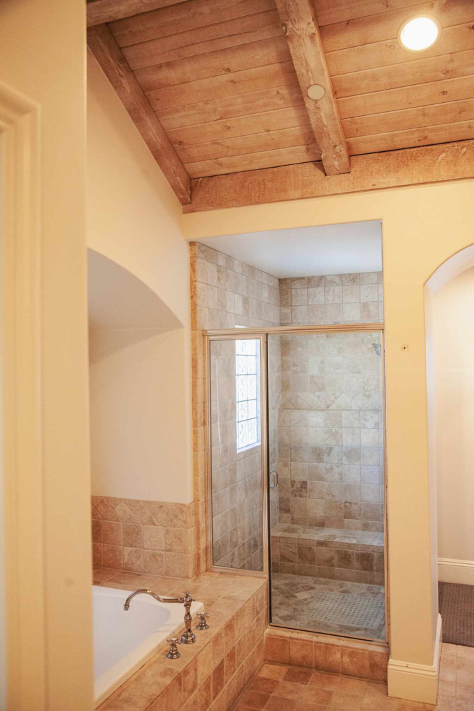 Spacious bathroom with tile shower, bathtub, and wood-beam ceiling.