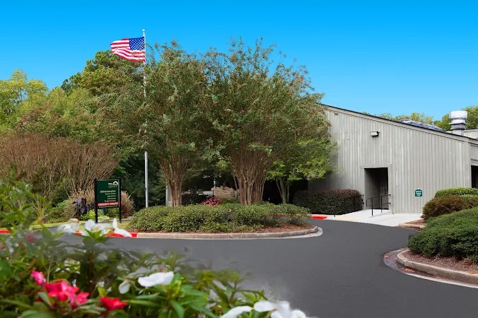 Facility entrance with driveway, flag, and greenery