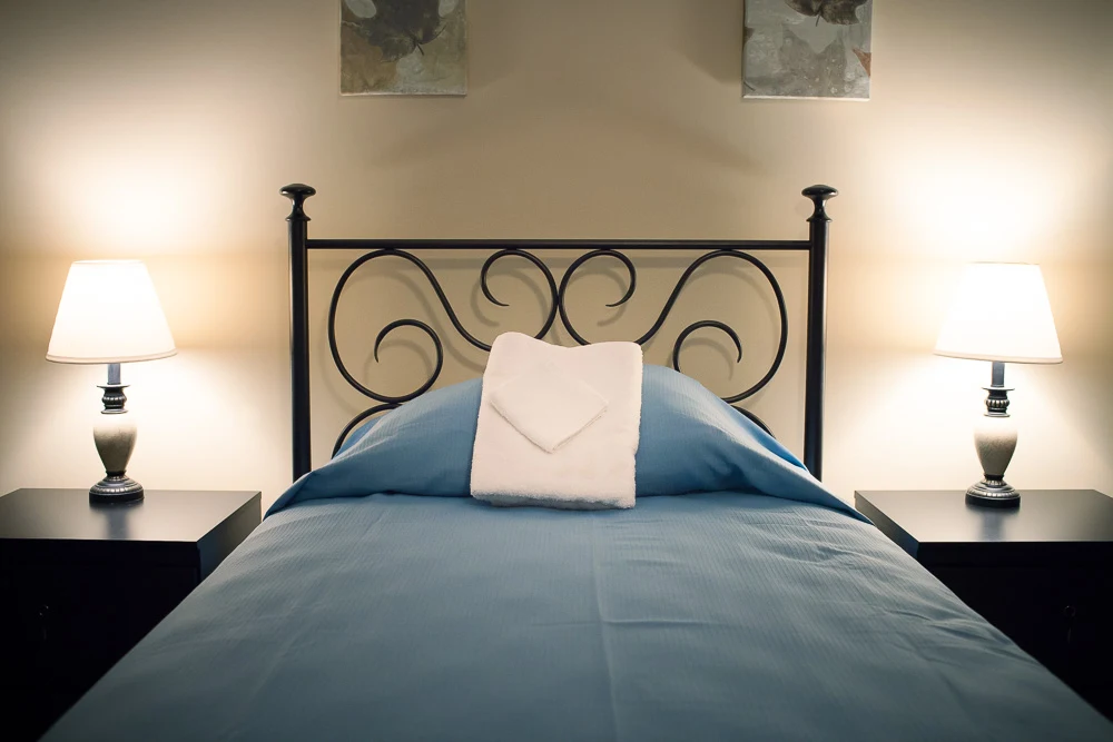 Clean semi-private bedroom with bed, lamps, and neutral decor