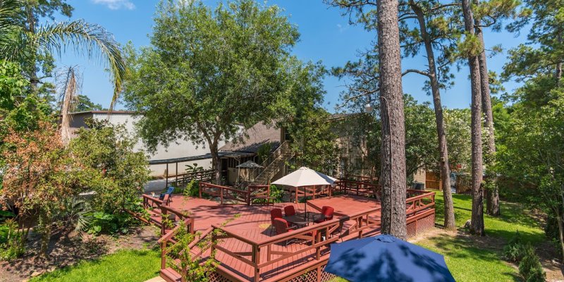 A spacious outdoor deck surrounded by trees, featuring cozy seating and umbrellas for shade, perfect for relaxation in a natural setting.