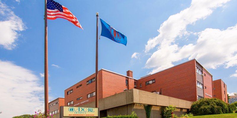  A bright day shows Adcare Hospital's welcoming exterior, framed by well-kept greenery and proudly flying the American and state flags.