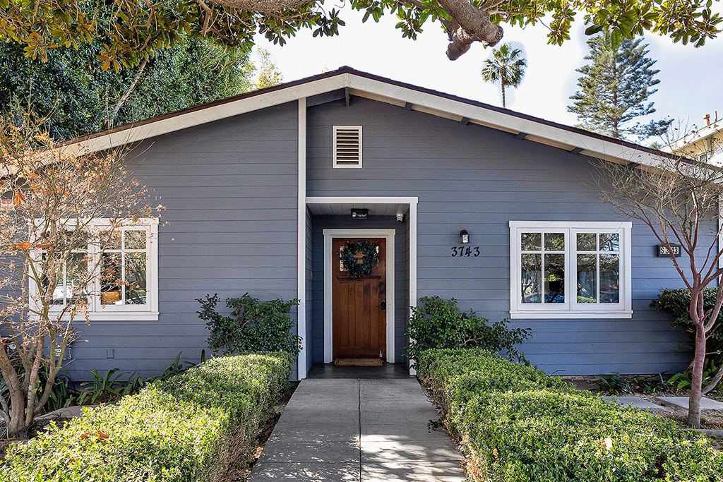 Blue exterior house with trimmed shrubs and central wooden front door