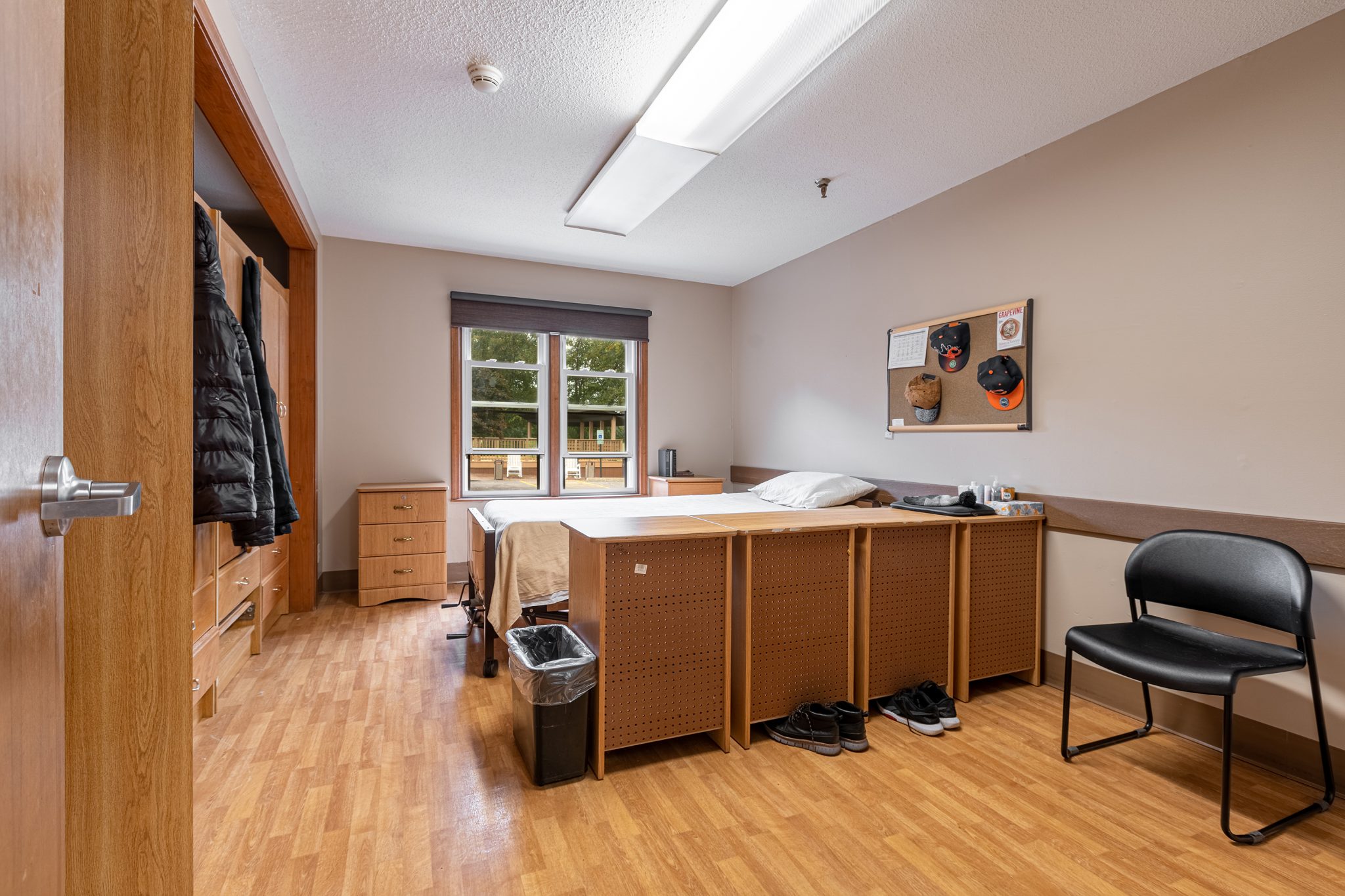 Neatly arranged resident bedroom with single bed, wooden storage units, and window view.