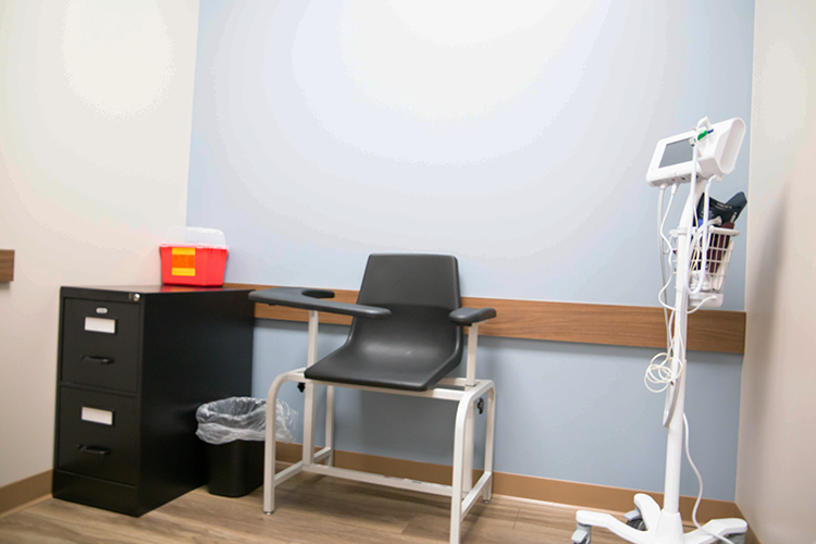 Clinical room with patient chair, vital-sign monitoring equipment, filing cabinet, and medical waste container