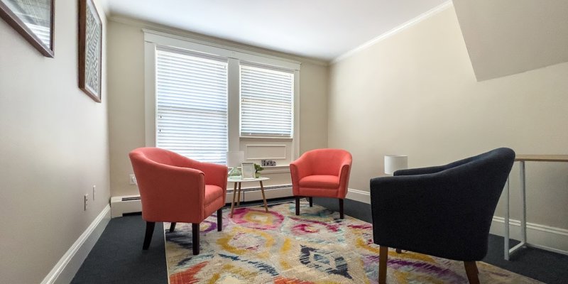 A cozy, well-lit room featuring two colorful armchairs and a vibrant rug, creating a welcoming and comfortable space for conversation or relaxation.