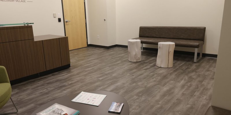  A comfortable waiting area with modern decor, featuring a cushioned bench, wooden side tables, and reading materials on a small table.