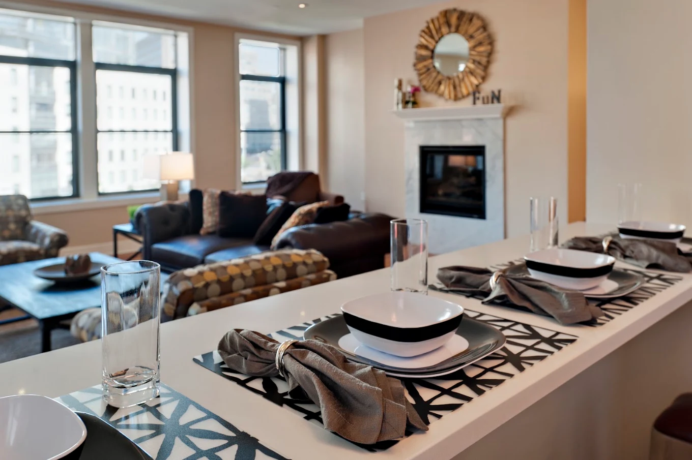 Modern living and dining area with place settings, lounge seating, fireplace, and large windows