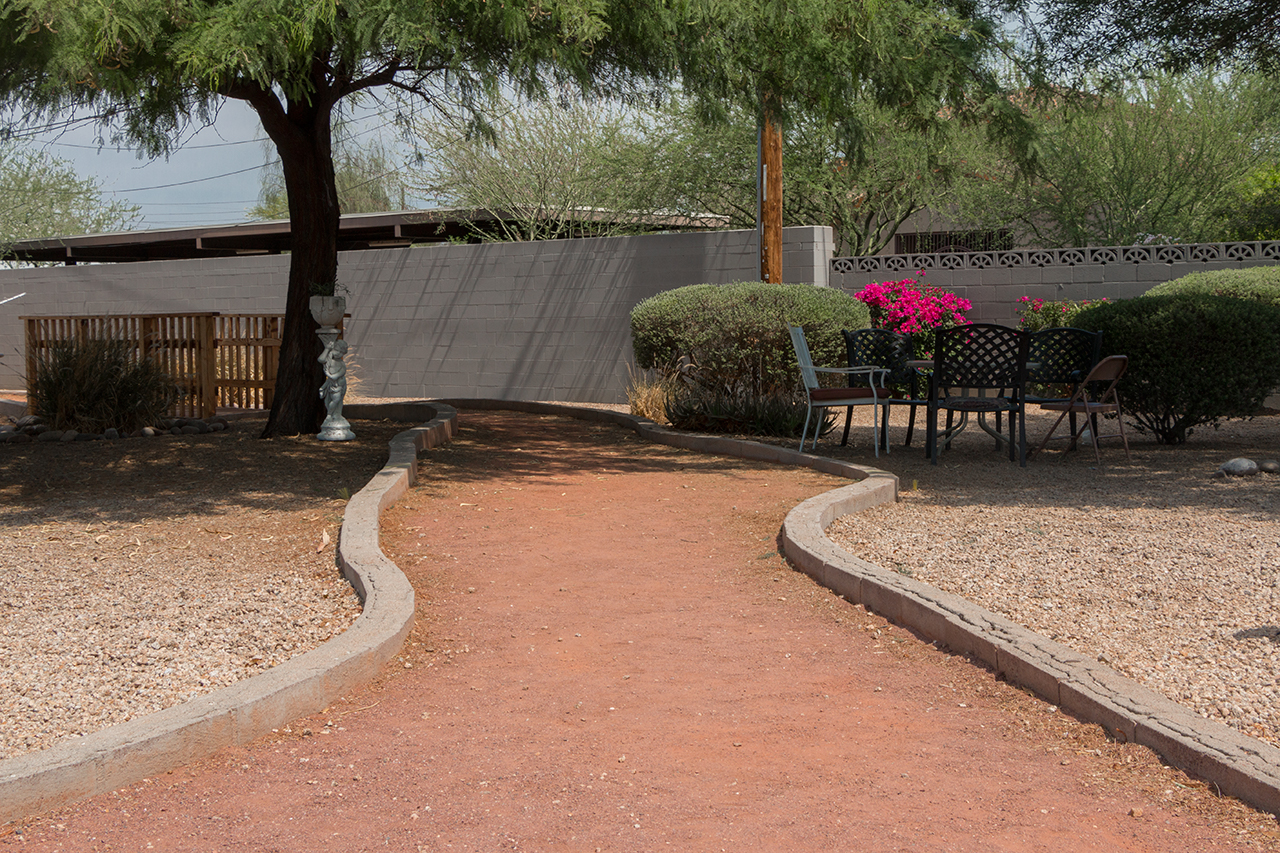 Patio tables and chairs under shade tree with garden wall