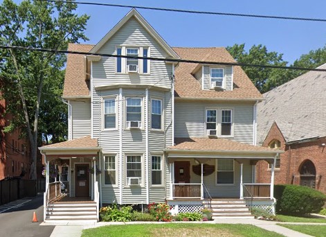 Large beige home with two porches and gable roof on sunny day