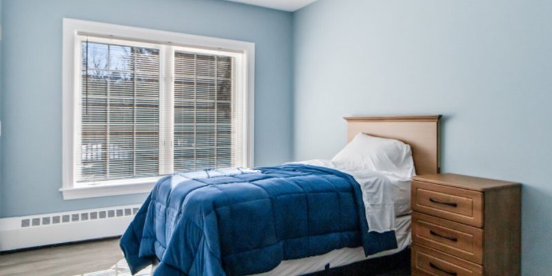 A simple, cozy room with a single bed, adorned with a blue comforter, and a wooden nightstand next to it.