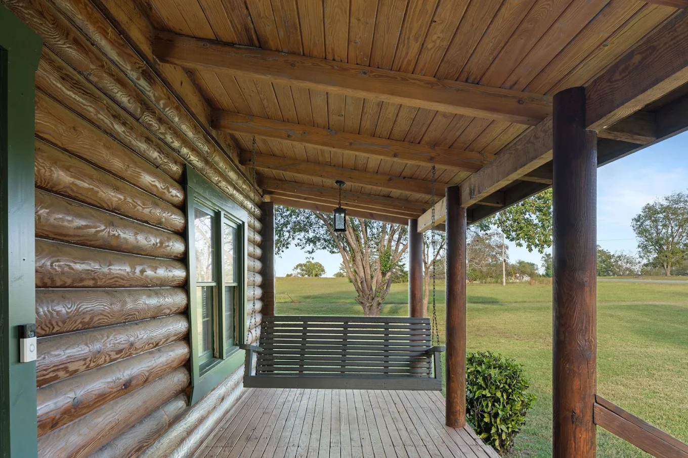 Covered log cabin porch with hanging swing overlooking open grounds