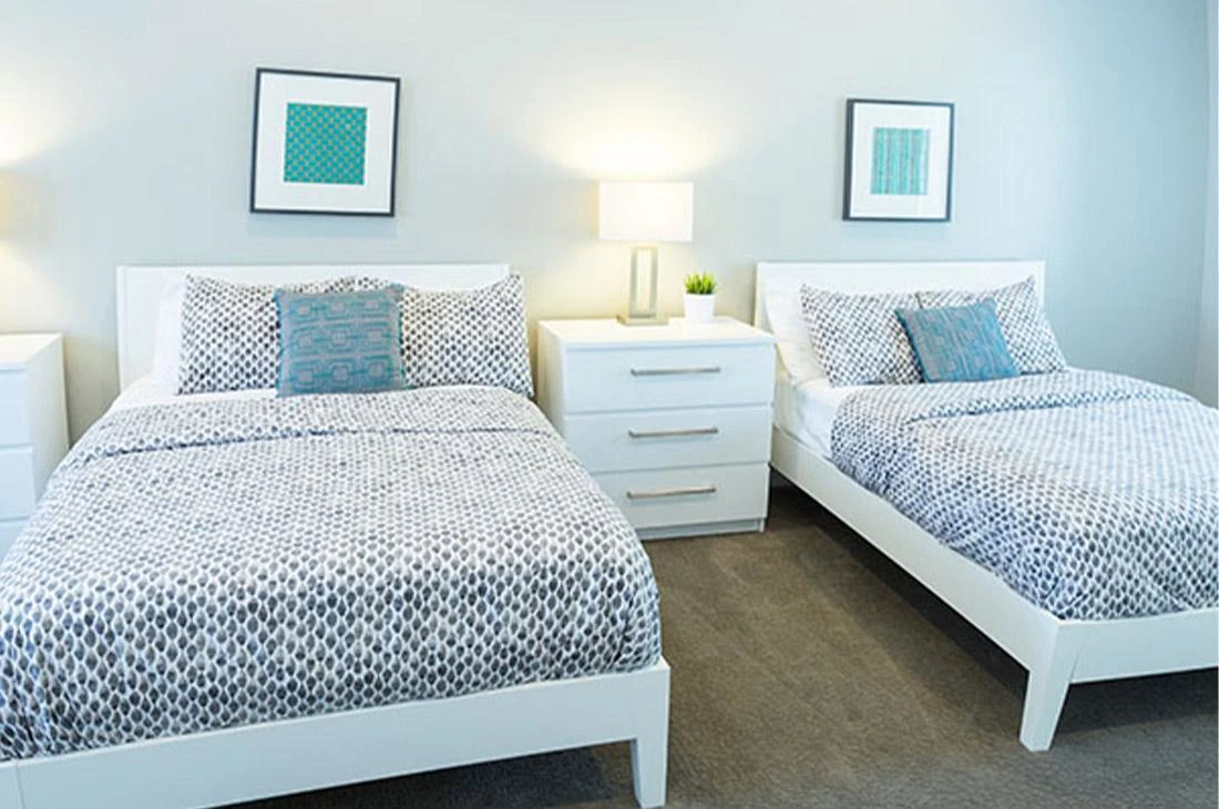 Two beds with white frames and geometric bedding in bright room