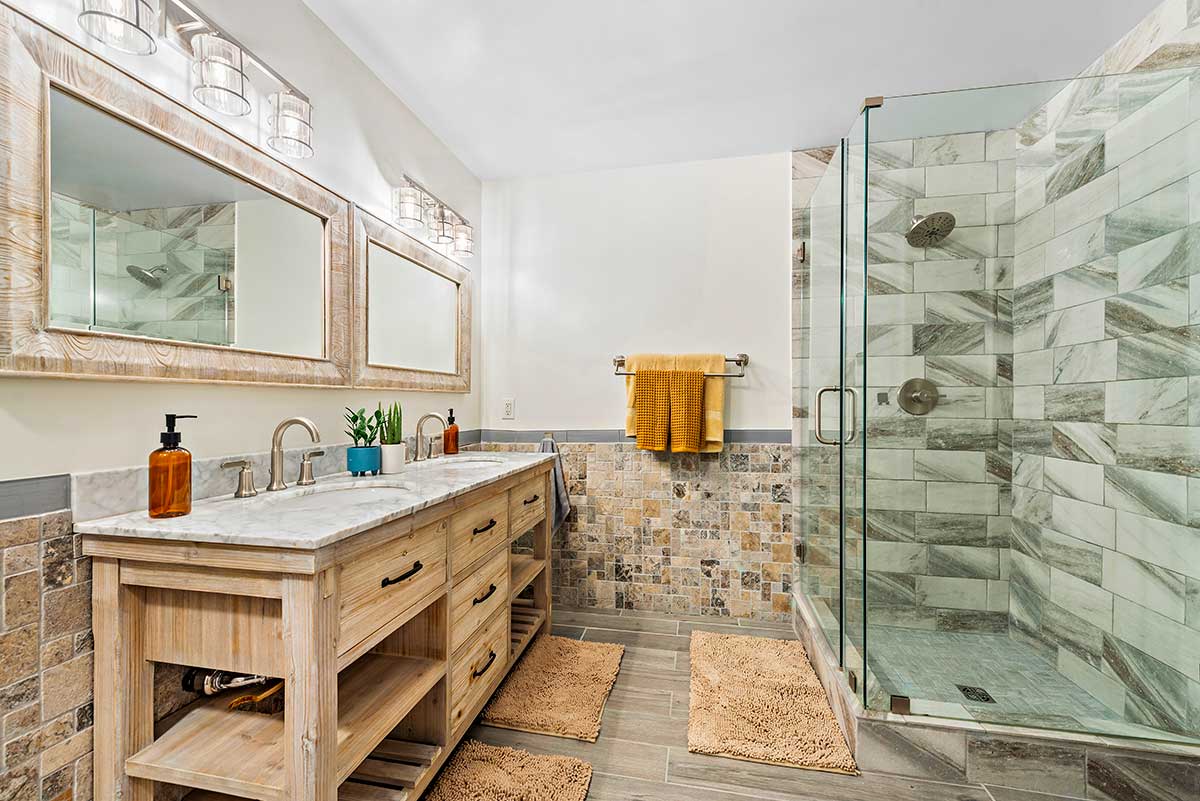 Spacious bathroom with granite vanity, wood cabinetry, and glass-enclosed tiled shower