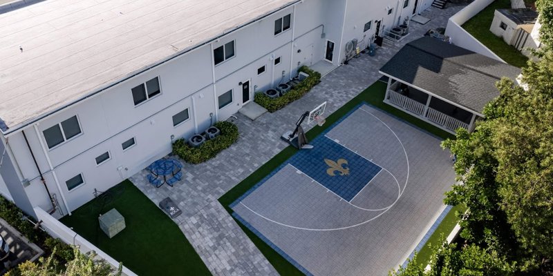 An aerial view of a clean, well-organized outdoor space featuring a basketball court, shaded seating area, and landscaped pathways.