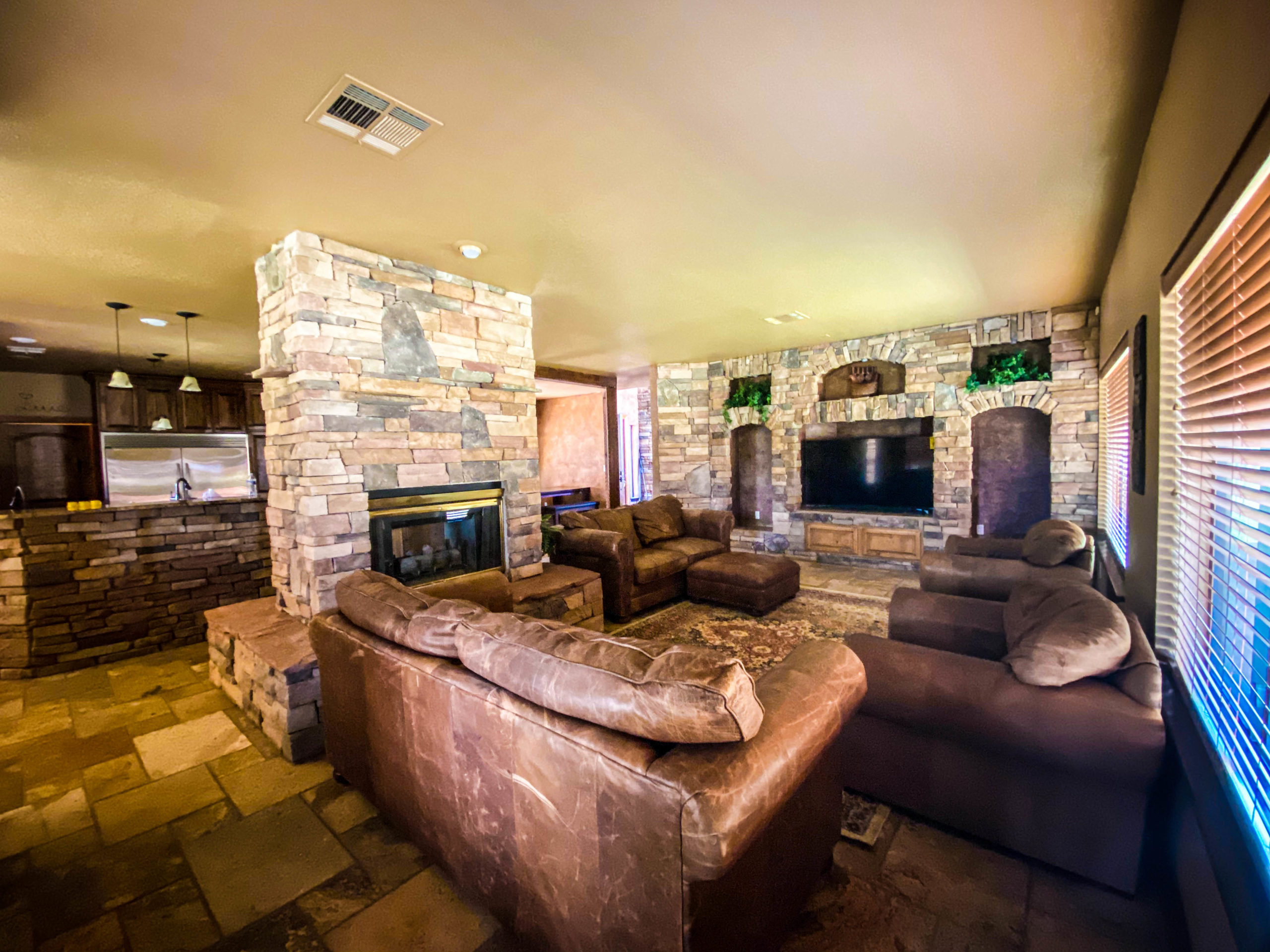 Inviting living room with multiple seating areas, stone fireplace, large TV, and rustic interior details