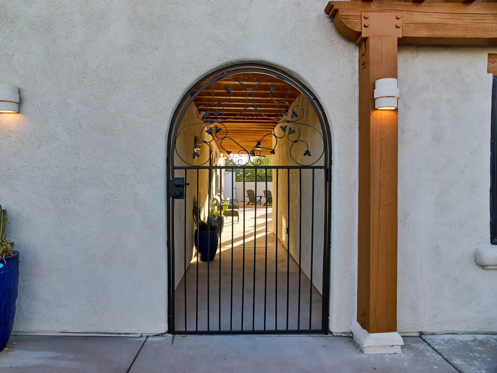 Arched metal gate opening to a shaded outdoor hallway