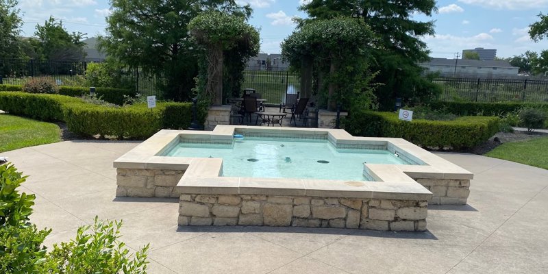  A serene outdoor area featuring a small, beautifully designed stone fountain surrounded by lush greenery, with a cozy seating area nearby.