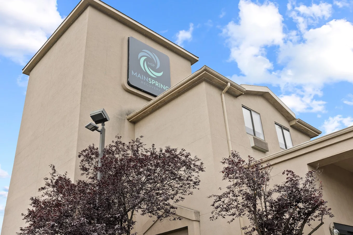 View of the Mainspring Recovery building with logo and trees in front