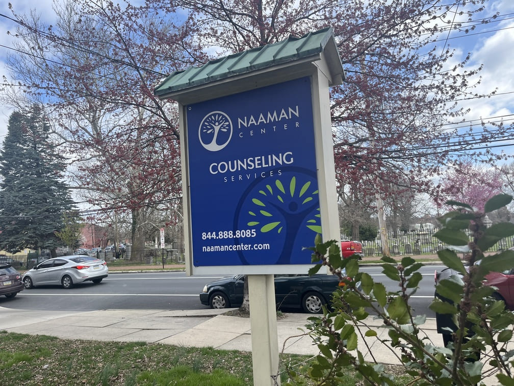 Street sign for Naaman Center with contact info and logo