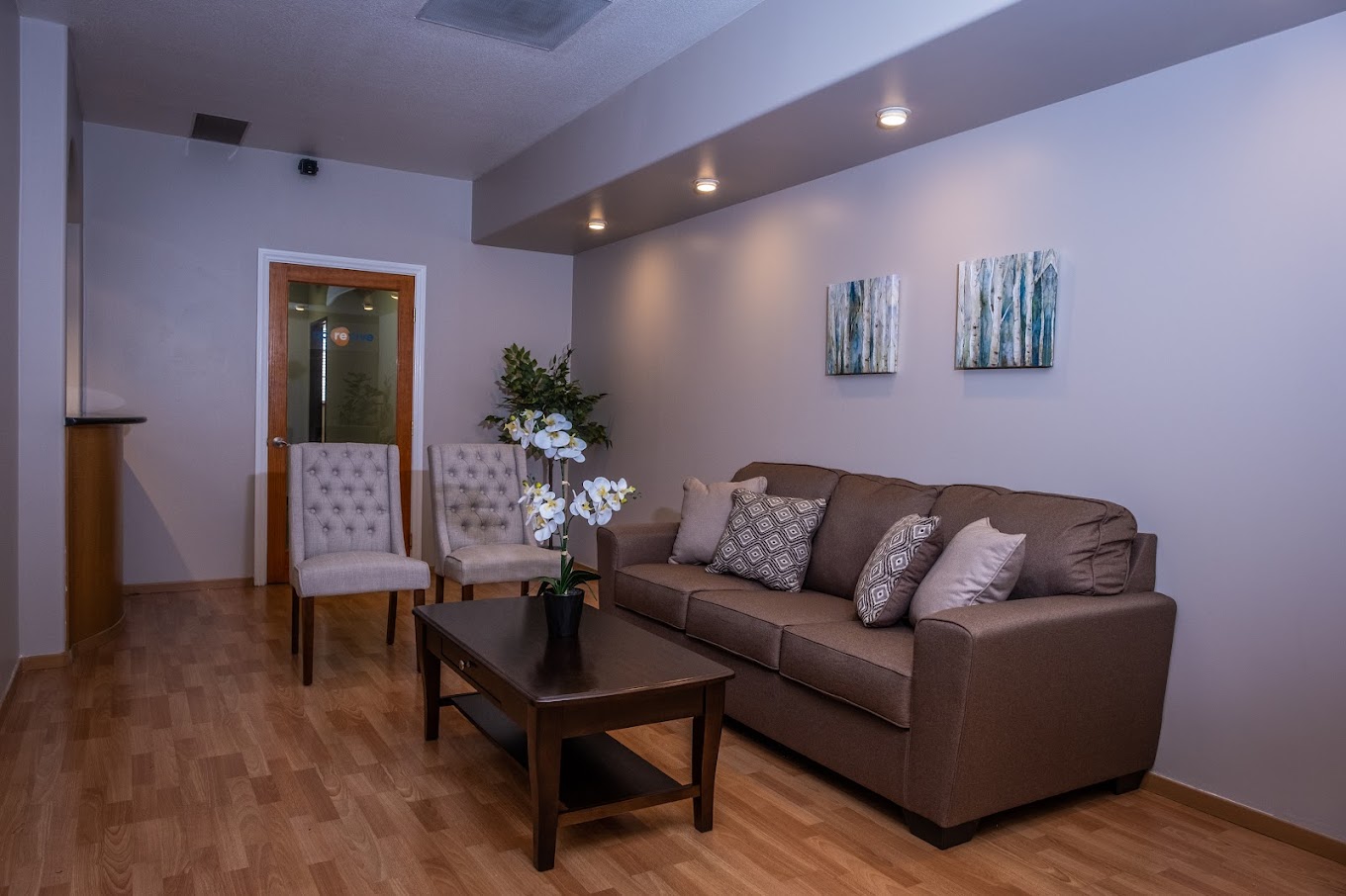 Cozy waiting area with a brown couch, two chairs, and warm lighting.