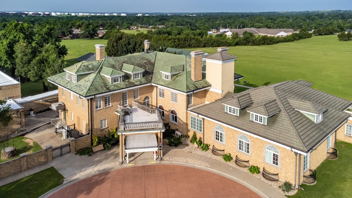An aerial view of a large brick Valley Hope of Cushing rehabilitation center with a green roof, surrounded by open fields and greenery.