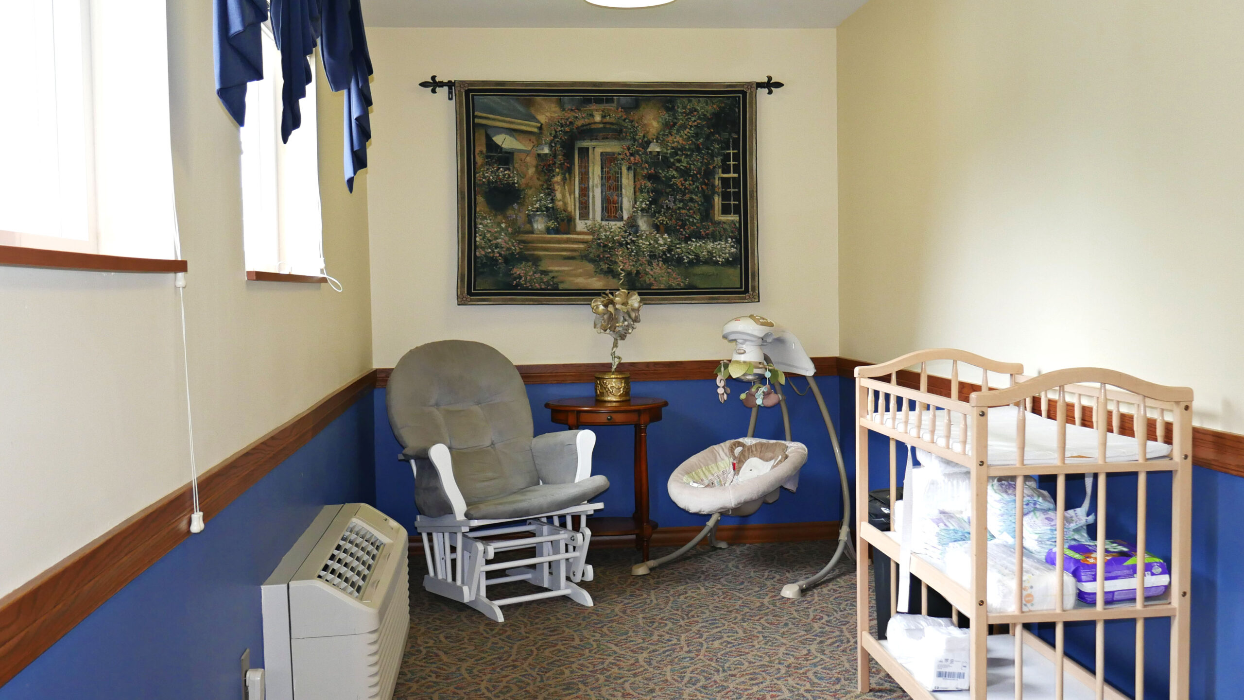 Glider chair, baby swing, and changing table in nursery space