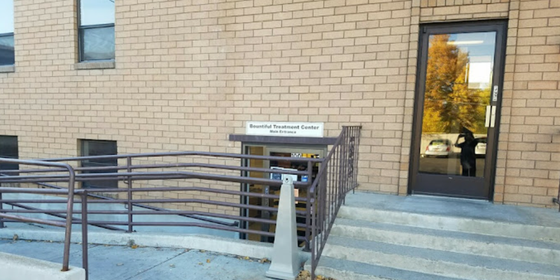 The entrance to a treatment center is accessible with a ramp and stairs, featuring a clean, brick facade and large windows for natural light.