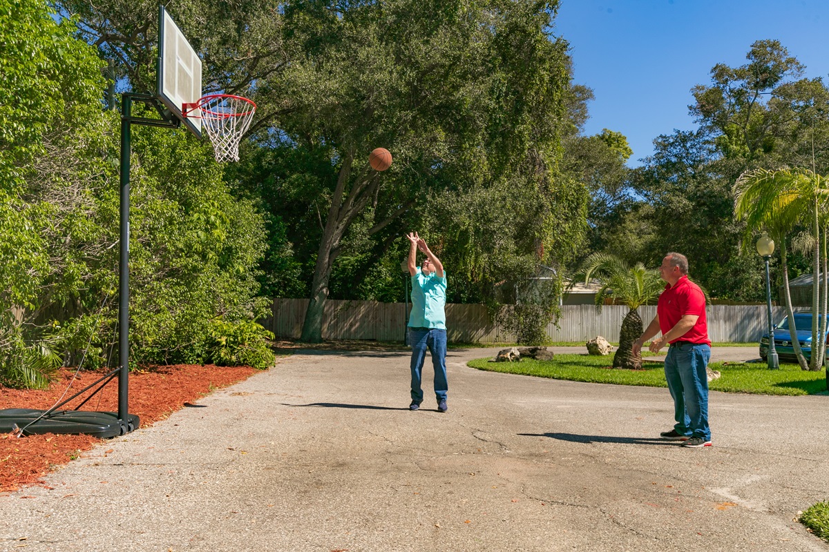 Two men playing basketball on outdoor court by trees