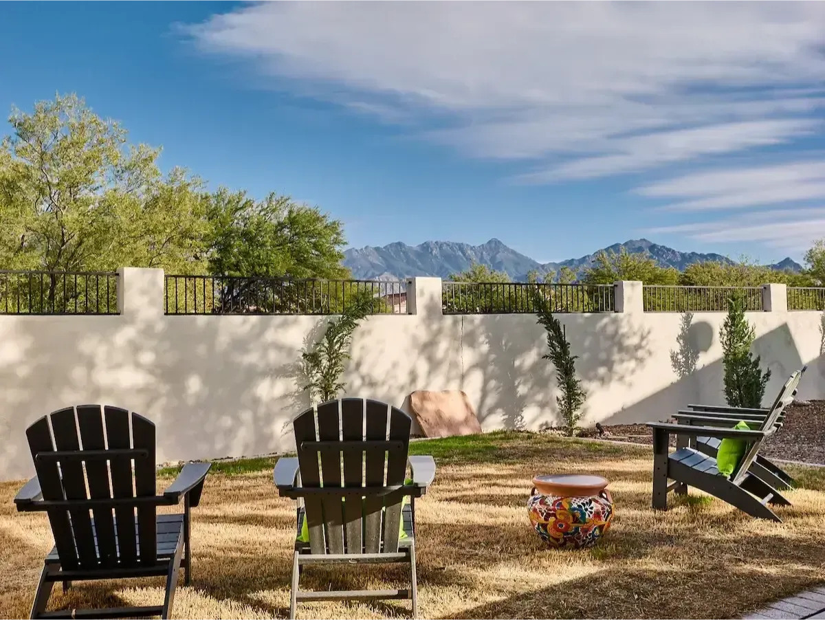 Chairs in a yard facing a mountain range and sunny sky.