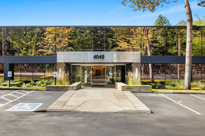 Modern mirrored building surrounded by trees and parking area