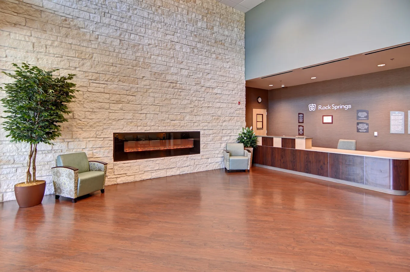 A spacious reception area with a modern wood-paneled desk, stone accent wall, indoor plants, and comfortable chairs for visitors