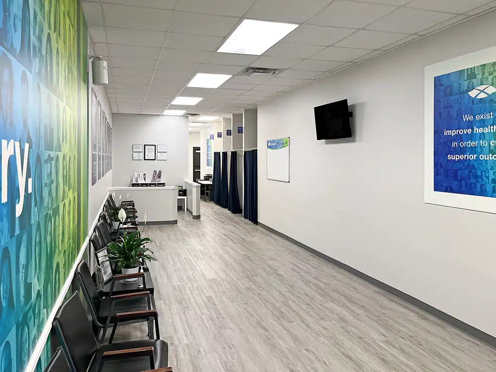 Waiting chairs along hallway with treatment rooms and TV