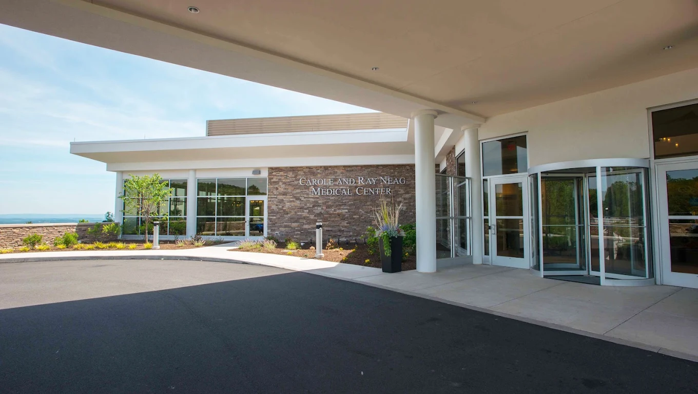 Covered entrance to the Carole and Ray Neag Medical Center with stone facade, glass doors, and landscaped surroundings
