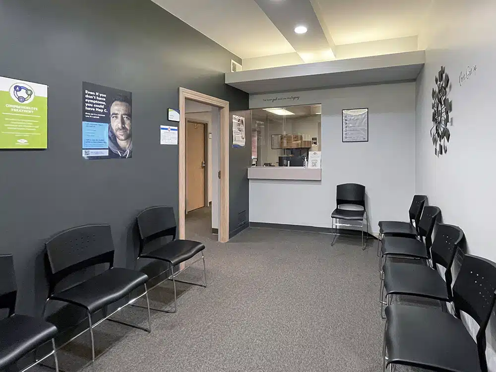 Waiting room with chairs along walls, reception window, and doorway leading to interior offices