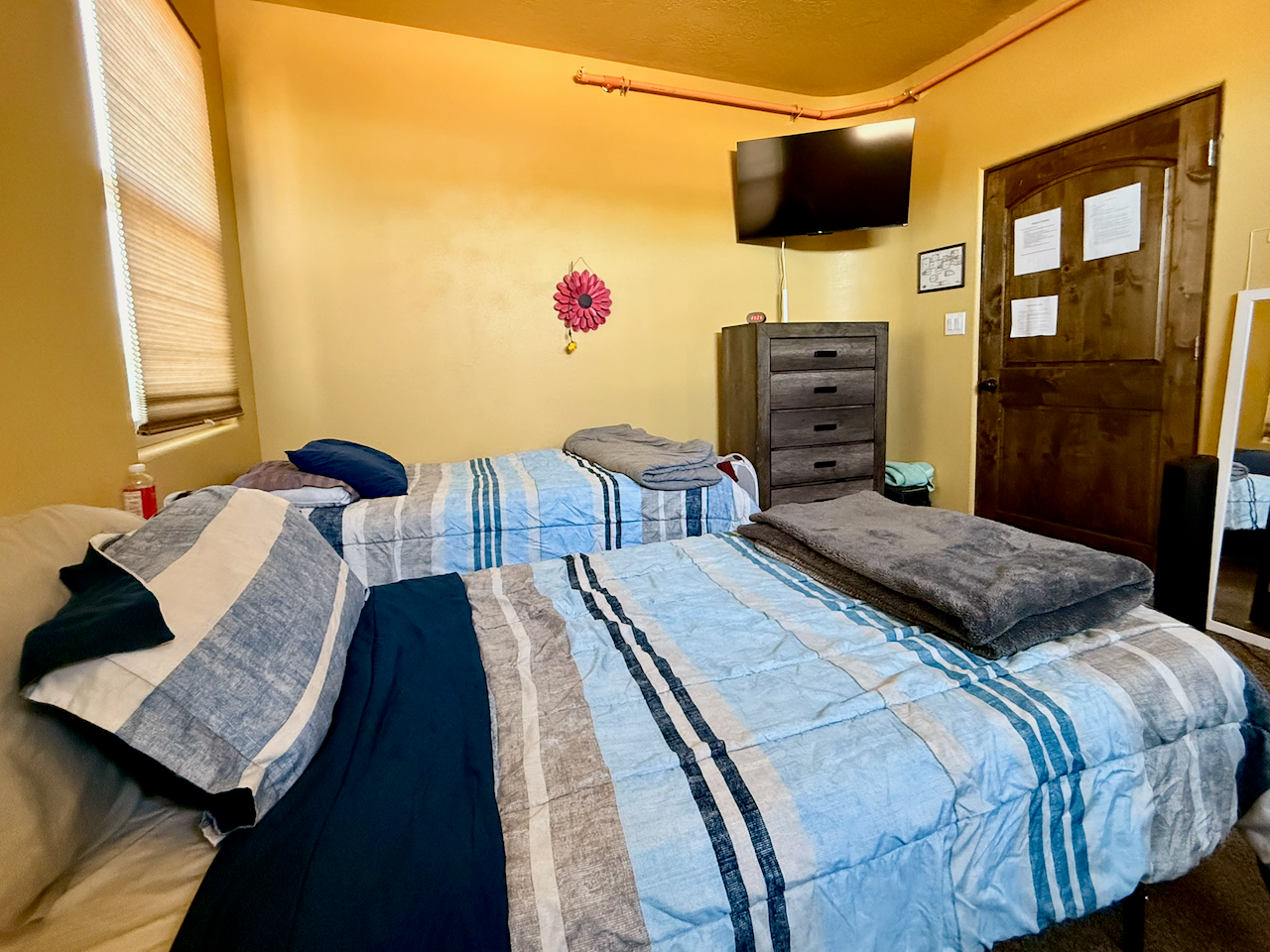 Shared bedroom with two beds, blue bedding, dresser, television, window, and wood door
