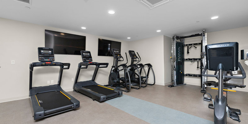  A modern fitness room equipped with treadmills, ellipticals, and strength-training machines. The space is bright, clean, and motivating for workouts.