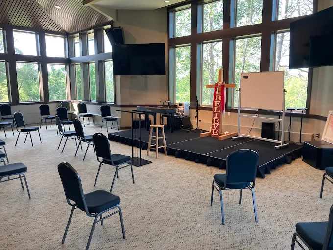 Bright chapel with stage, cross, and chairs arranged in a circle