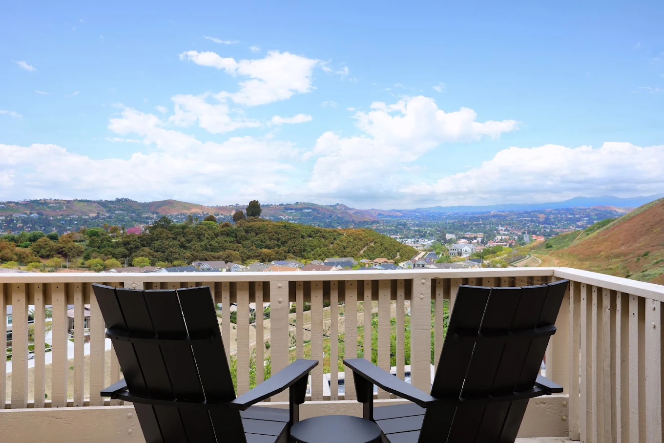 Outdoor balcony with two Adirondack chairs overlooking rolling hills, residential neighborhoods, and a wide blue sky