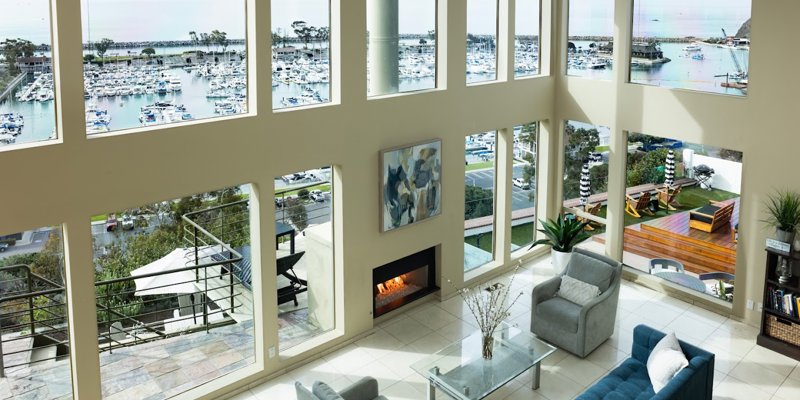 A luxurious, open living space with floor-to-ceiling windows offering stunning views of a marina, complemented by modern furniture and a cozy fireplace.