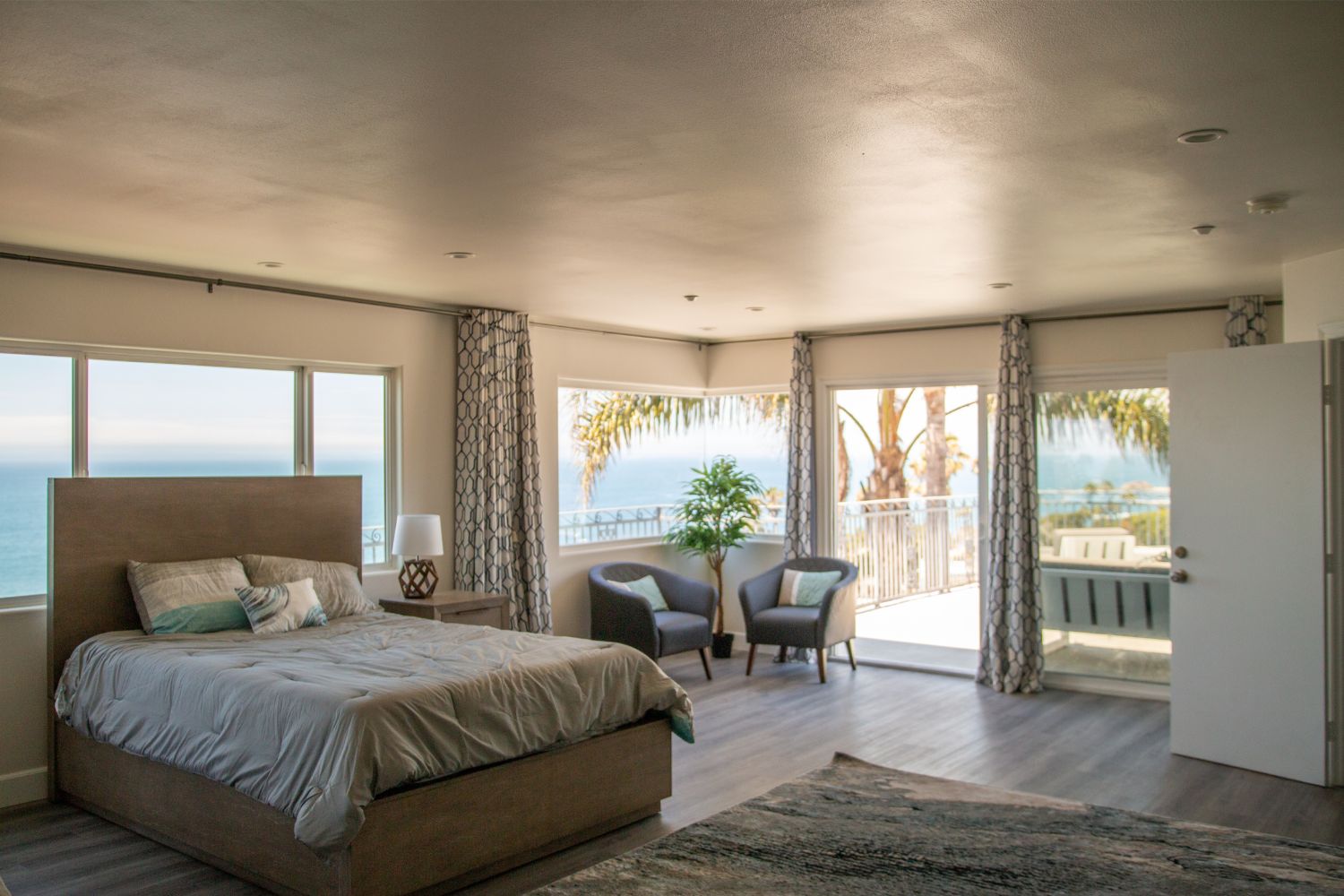 Bright, spacious bedroom with ocean views, featuring a cozy bed, modern decor, and comfortable seating by large windows that let in natural light.