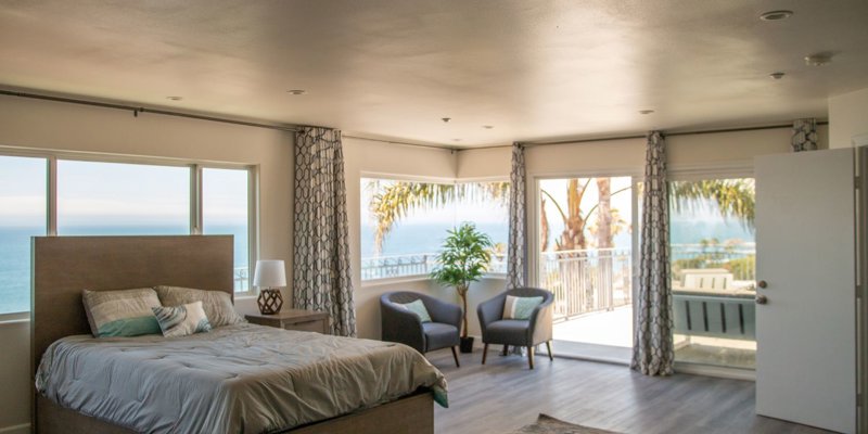 Bright, spacious bedroom with ocean views, featuring a cozy bed, modern decor, and comfortable seating by large windows that let in natural light.