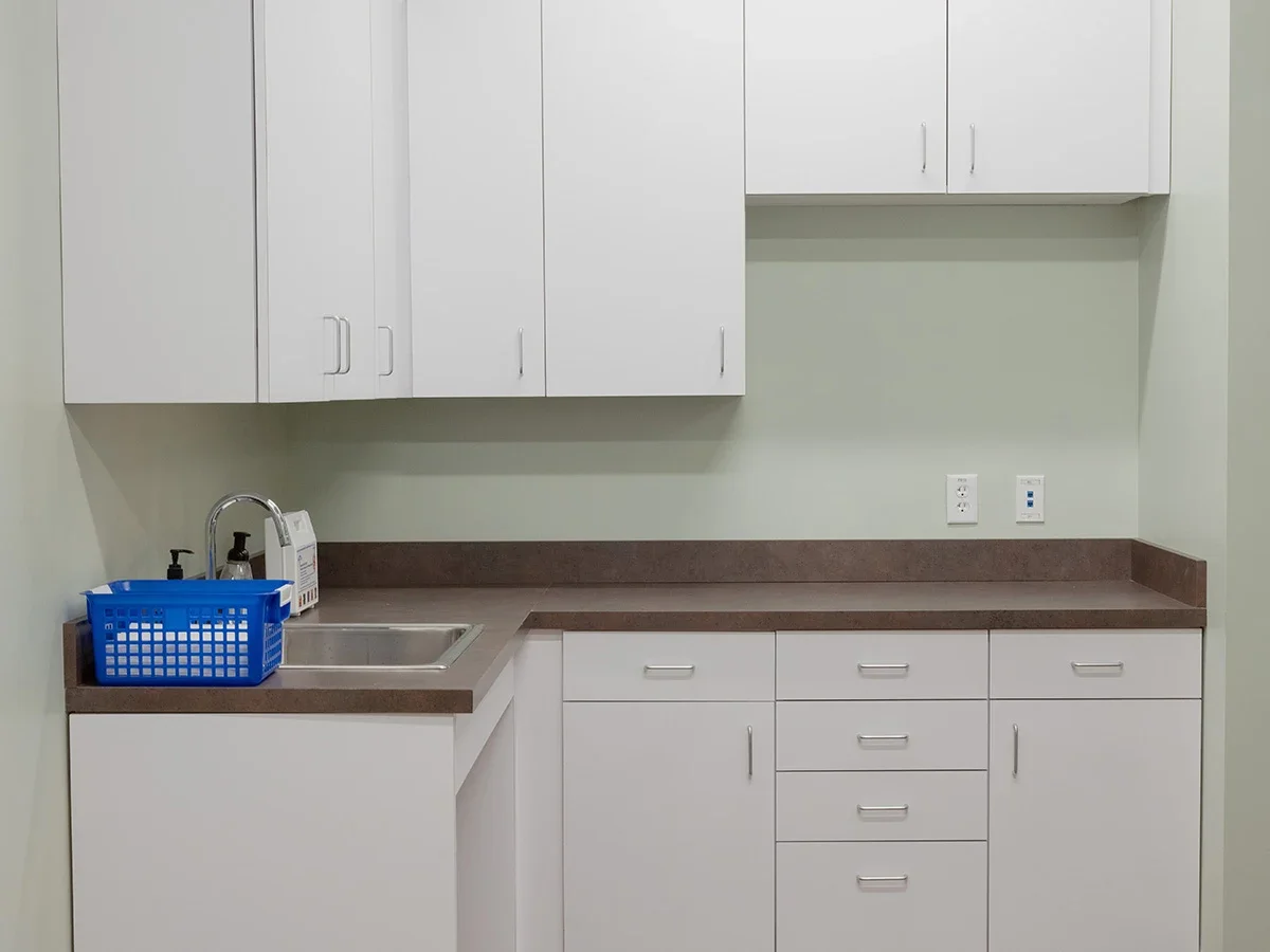 Clean medical prep area with cabinets, sink, and countertop space